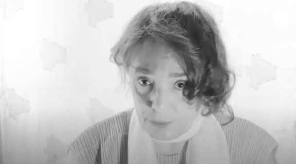 poet looking directly at us, dark hair brushed to one side, a light scarf, soft sweater, intense gaze
