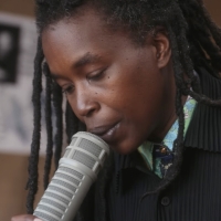 poet with a microphone to their mouth, long dreadlocks falling down, a sharp blue suit, focus