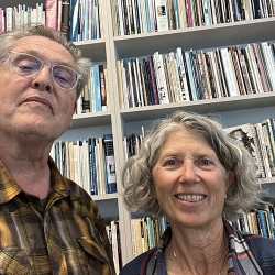 two poets standing in front of a wall of books trying to smile