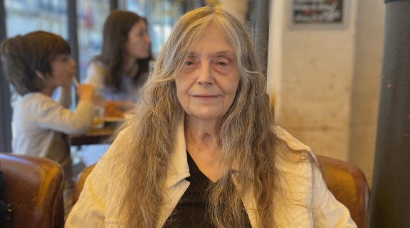 poet in long grey hair, black t-shirt, white buttoned shirt, smiling in a cafe, two children in the background