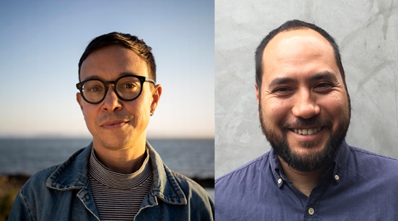 Two men, each looking straight ahead: both have short cropped dark hair, the one on the left in a turtleneck, jacket, wearing round glasses, on the right, the other wears a blue shirt and wide smile