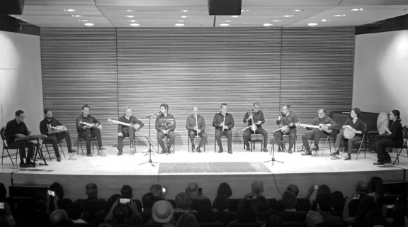an ensemble of musicians on stage playing traditional Persian instruments before a live audience