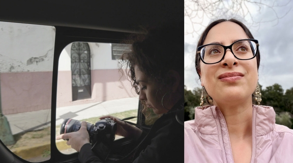 a woman with a camera, in shadow within a car with street scene through the window glass; a poet with eyeglasses, long earrings, dark hair pulled back, light pink top and cloudy sky with branches behind